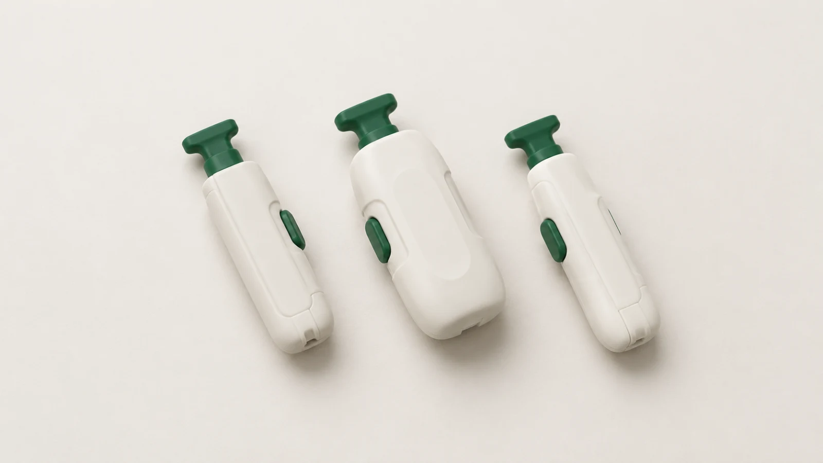 Illustration of three capped single-use safety lancets with off-white bodies and green caps and side buttons, lying on an off-white surface.